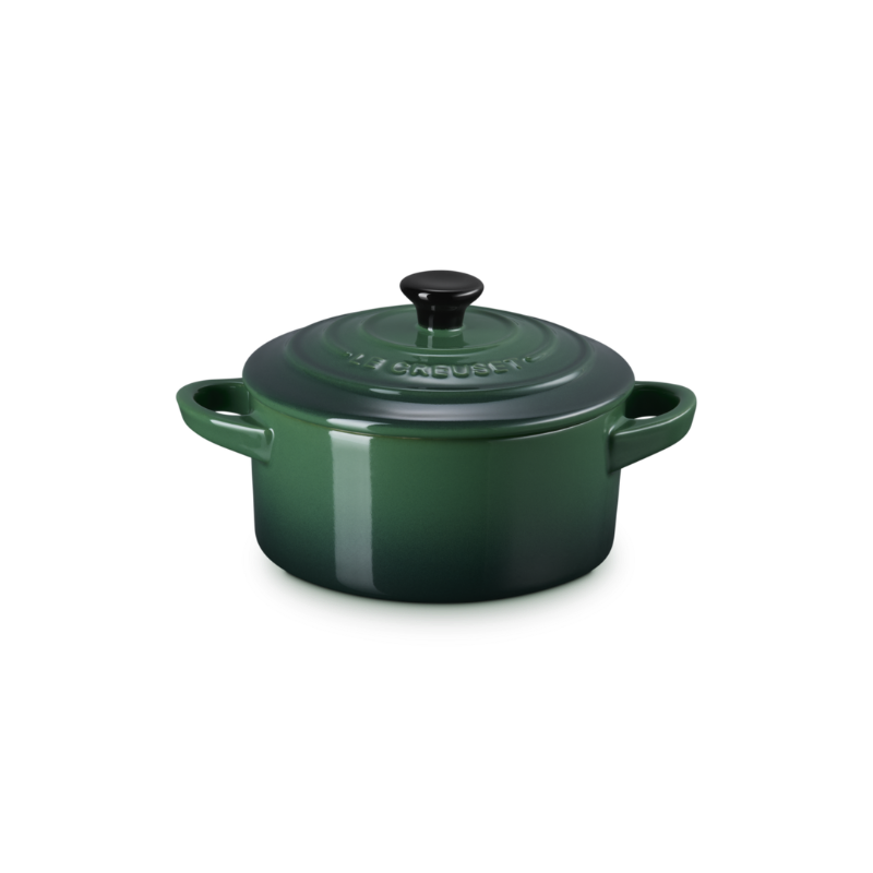 Green enameled cast iron cocotte with a black lid on a white background