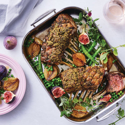 Roasted lamb with vegetables on a platter, served with a side dish of figs and peas.