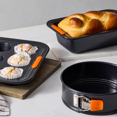 Set of bakeware including a muffin tray, loaf pan, and springform pan on a kitchen counter.