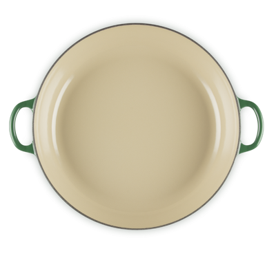 Beige enamel pan with green handles on a white background