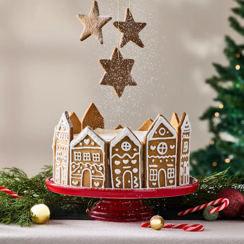 Decorative gingerbread house display with star-shaped ornaments on a stand, Christmas tree in the background.