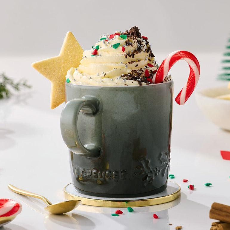 Hot chocolate in a mug with whipped cream, a candy cane, and a star-shaped cookie on a festive background.