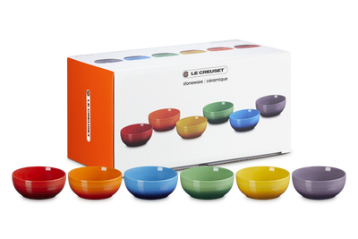 Set of colorful bowls in front of Le Creuset packaging on a white background
