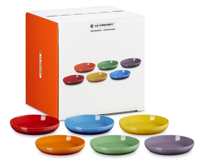 Set of colorful ceramic bowls in front of Le Creuset packaging.