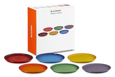 Set of colorful plates with Le Creuset packaging on a white background