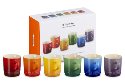 Set of colorful mugs in front of a Le Creuset box on a white background