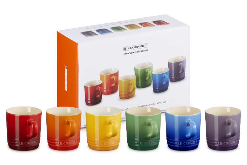 Set of colorful mugs in front of a Le Creuset box on a white background
