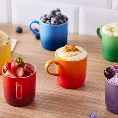 Colorful mugs filled with various desserts on a wooden table.