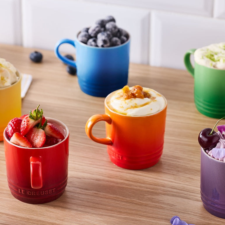 Colorful mugs filled with various desserts on a wooden table.