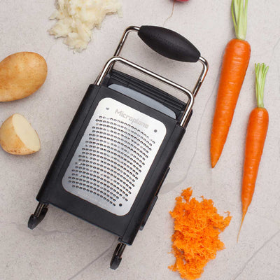 Black box grater with carrots and a carrot shreds on a light surface