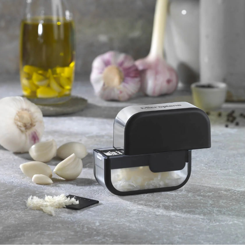 Garlic press on a kitchen counter with garlic cloves and oil in the background