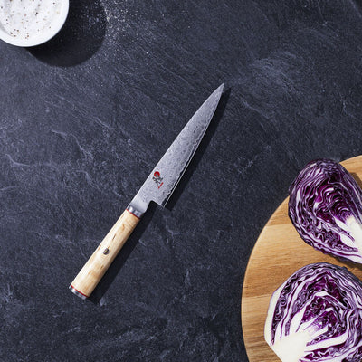 Chef's knife with a wooden handle on a dark surface next to a cutting board with purple cabbage.
