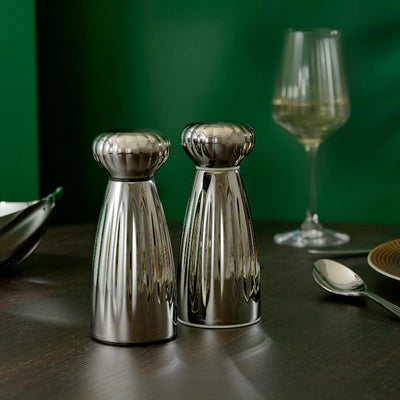 Two metallic salt and pepper shakers on a table with a glass of white wine in the background.