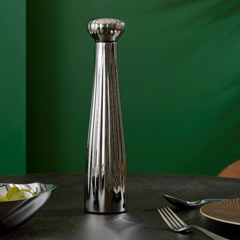 Silver salt shaker on a dark surface with a green background