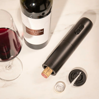 Wine bottle, wine glass, and electric wine opener on a white surface