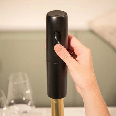 Hand holding a black wine bottle opener with a blurred background